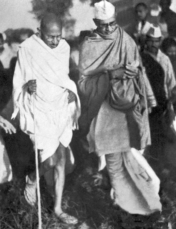 चित्र 2। गांधी जी (बाएँ) महादेव देसाई (दाएँ) के साथ, सेवाग्राम आश्रम में टहलते हुए। चित्र: अज्ञात छायाकार / Wikimedia Commons / Public Domain